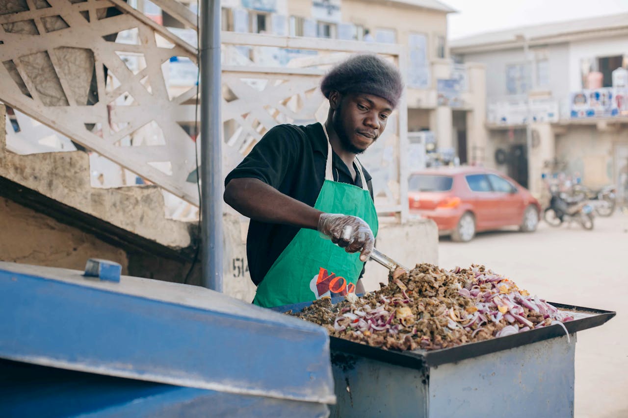 our-story-01 Street vendor preparing jollof rice on a busy urban street, showcasing culinary culture.