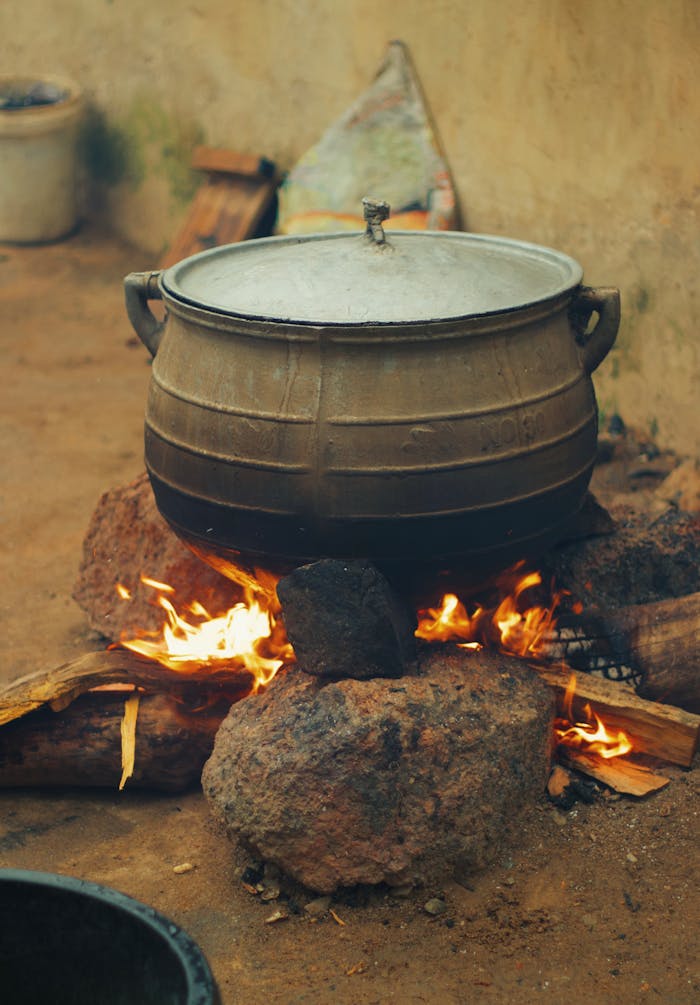 A large traditional pot sits over a fire, cooking a meal in Nigeria. Rural setting.